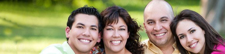 Picture of a smiling family with a son, mother, father, and daughter with green grass in the background. 